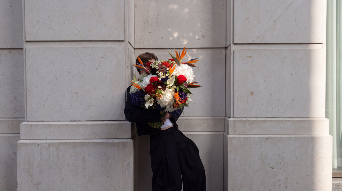 Model hiding behind an oversized autumn bouquet against a stone wall